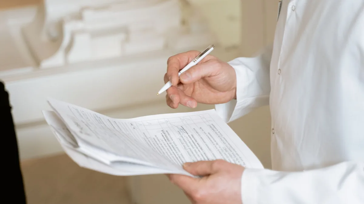From above of crop anonymous plump female doctor in disposable gloves working at table with paper on clipboard — Illustration accompanying coverage of the CagriSema phase 3 trials registry update from Novo Nordisk