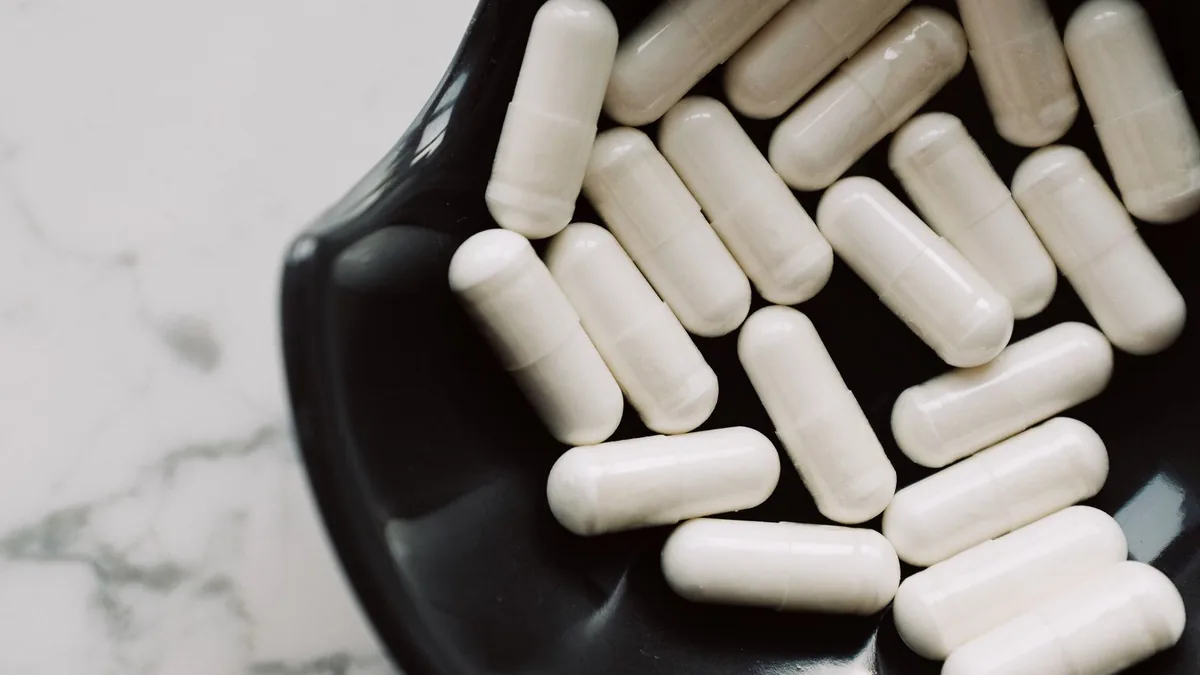 A detailed shot of white capsules in a black bowl, highlighting healthcare concerns. — Glass multi-dose injection vial on a clinical counter with a pharmacy label showing a lot number