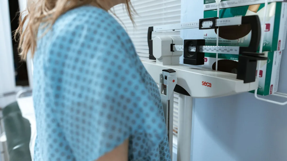 Adult female using a medical weighing scale in a healthcare setting. — Illustration accompanying a report on GLP-1 non-responders and research into predicting response to incretin therapy