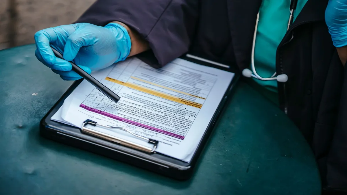 From above of crop anonymous plump female doctor in disposable gloves working at table with paper on clipboard — Illustration accompanying coverage of the semaglutide opioid use disorder trial now recruiting participants