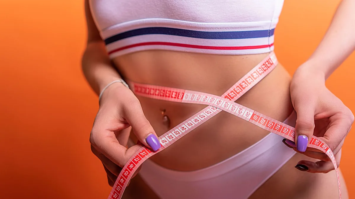 Close-up of a woman in underwear measuring her waist with a tape measure, fitness concept. — Illustration accompanying coverage of a tirzepatide abdominal fat study from the SURMOUNT-J trial